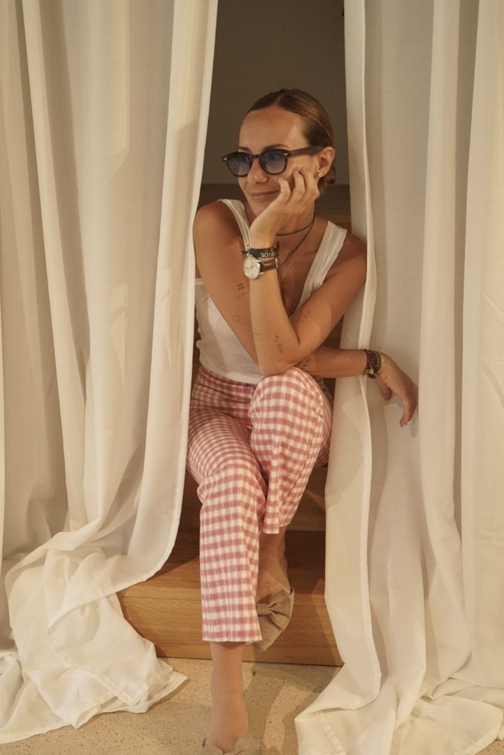 Mina sitting between white curtains, wearing sunglasses and pink gingham trousers