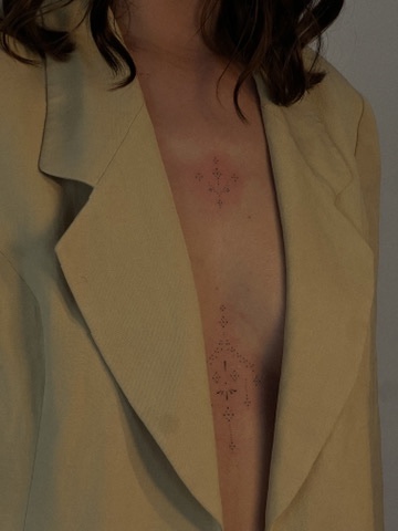 Fine line ornamental tattoo along the sternum
